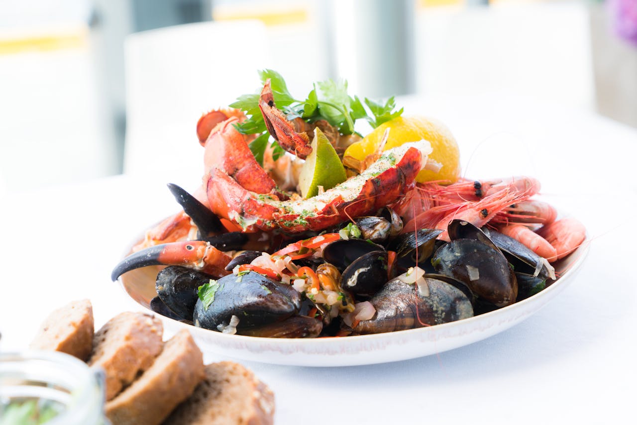 heros-img A vibrant seafood platter featuring lobster, shrimp, mussels, and lemon on a white plate.